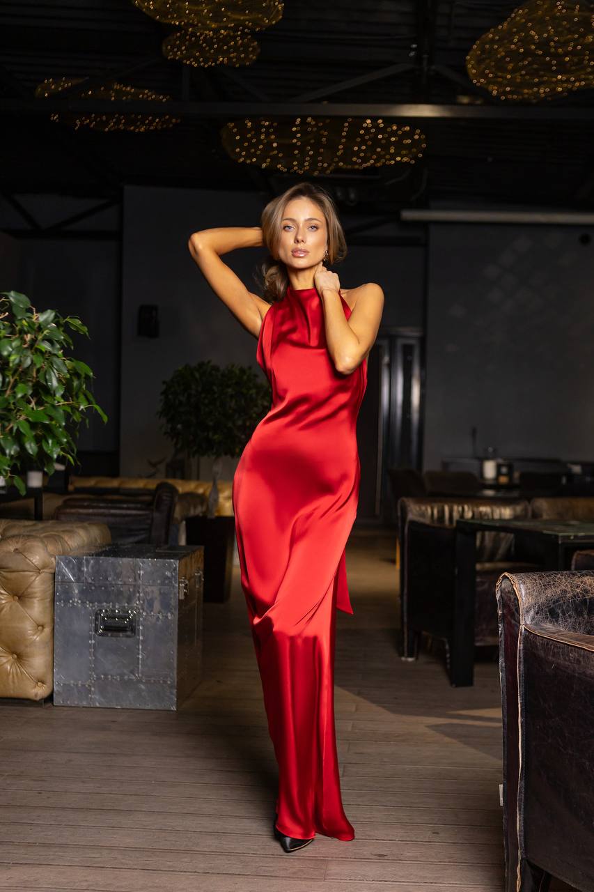 Woman in a red dress posing in a dimly lit room with plants and furniture.