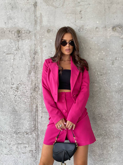 Woman in a bright pink outfit standing against a concrete wall.