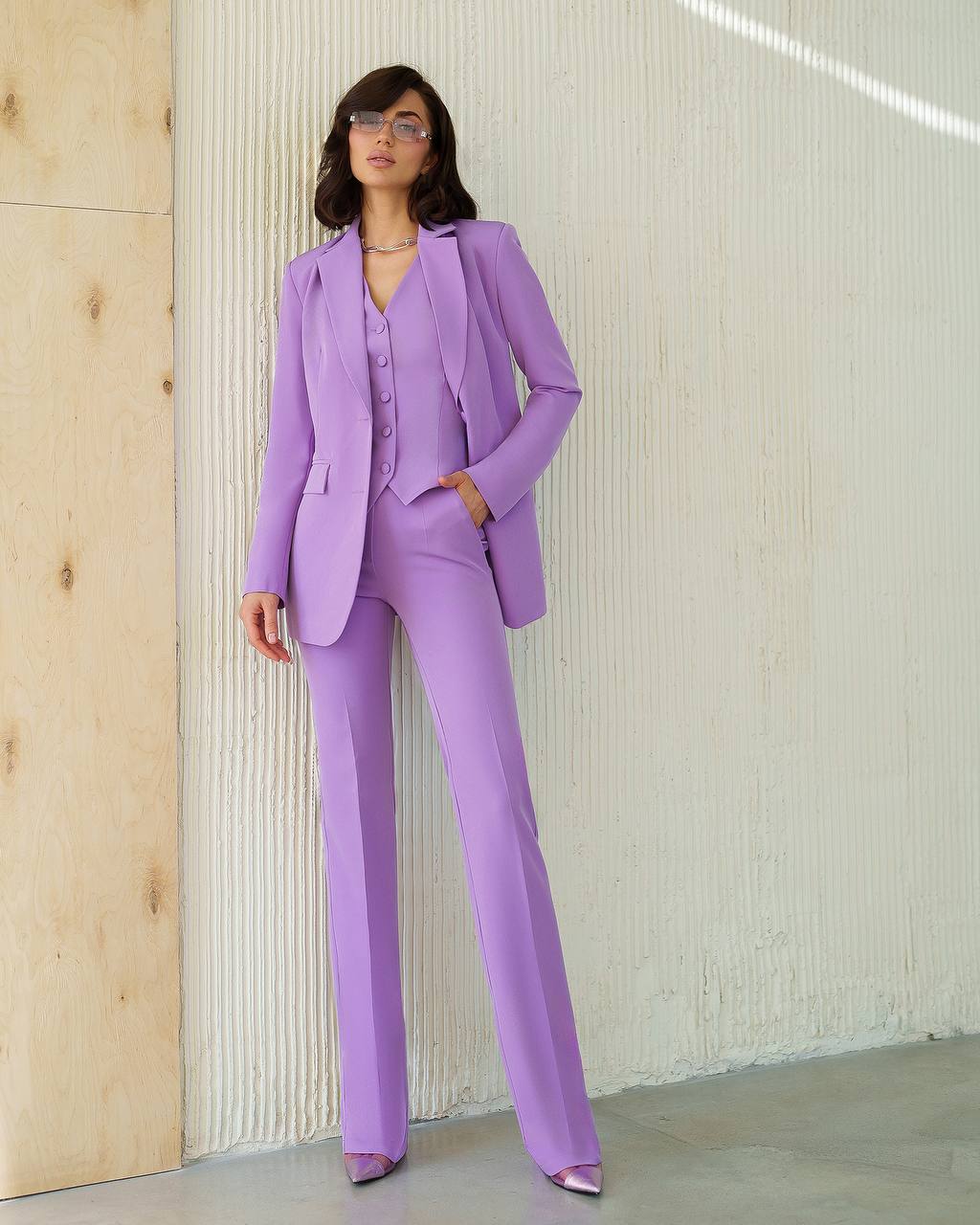 Woman wearing a purple suit standing against a light-colored wall.