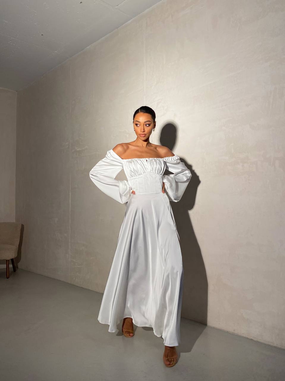 Woman wearing a white off-shoulder dress in a minimal room.
