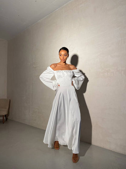 Woman wearing a white off-shoulder dress in a minimal room.