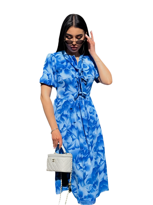 Woman wearing a blue floral dress holding a white handbag on a white background