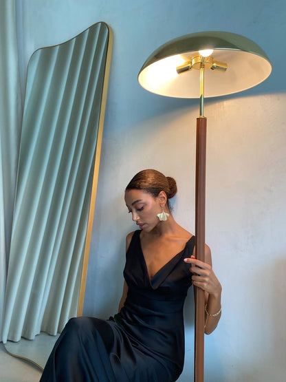 Woman in a black dress holding a gold floor lamp against a light blue wall.
