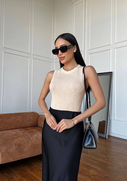 Woman in a stylish outfit with a cream top and black skirt, holding a blue handbag indoors.