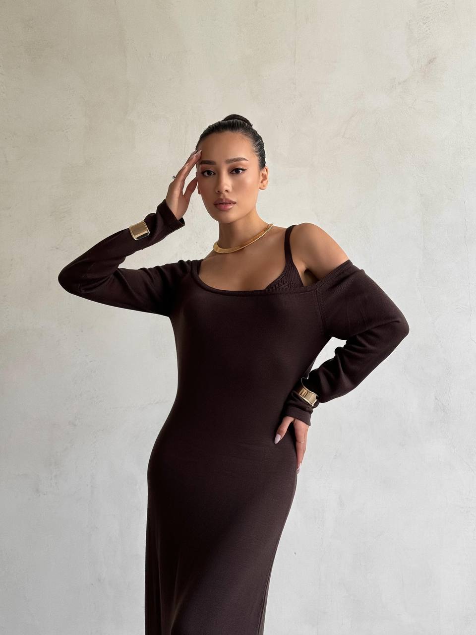 Woman wearing a brown dress with long sleeves and cut-out shoulders against a plain background