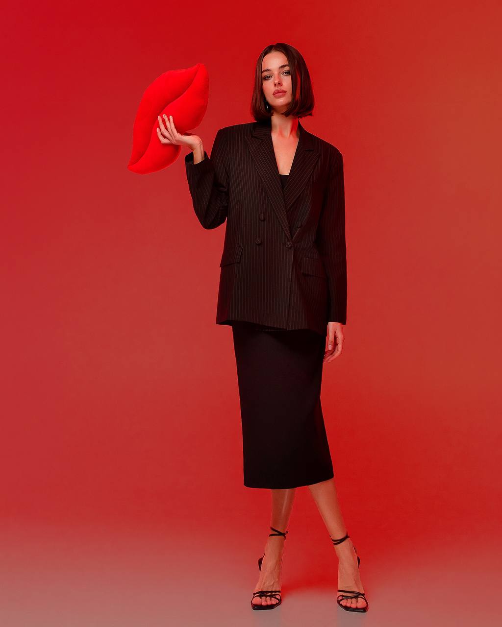 Woman in a black suit holding a red pillow against a red background