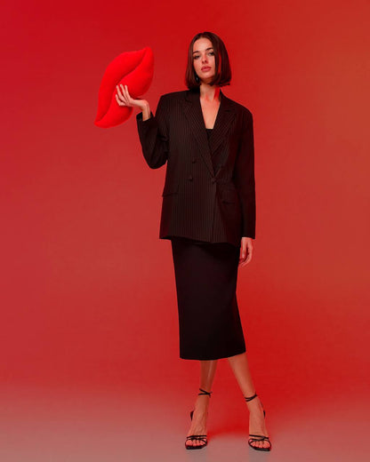 Woman in a black suit holding a red pillow against a red background