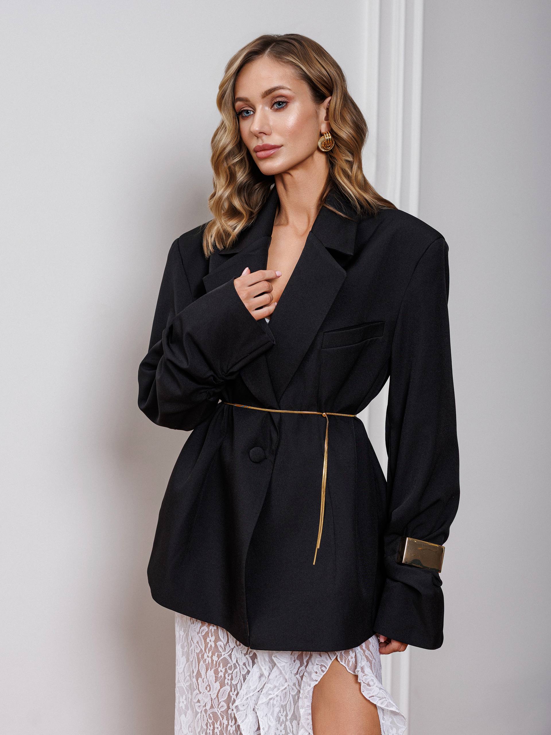 Woman wearing a black blazer with gold accents against a plain background