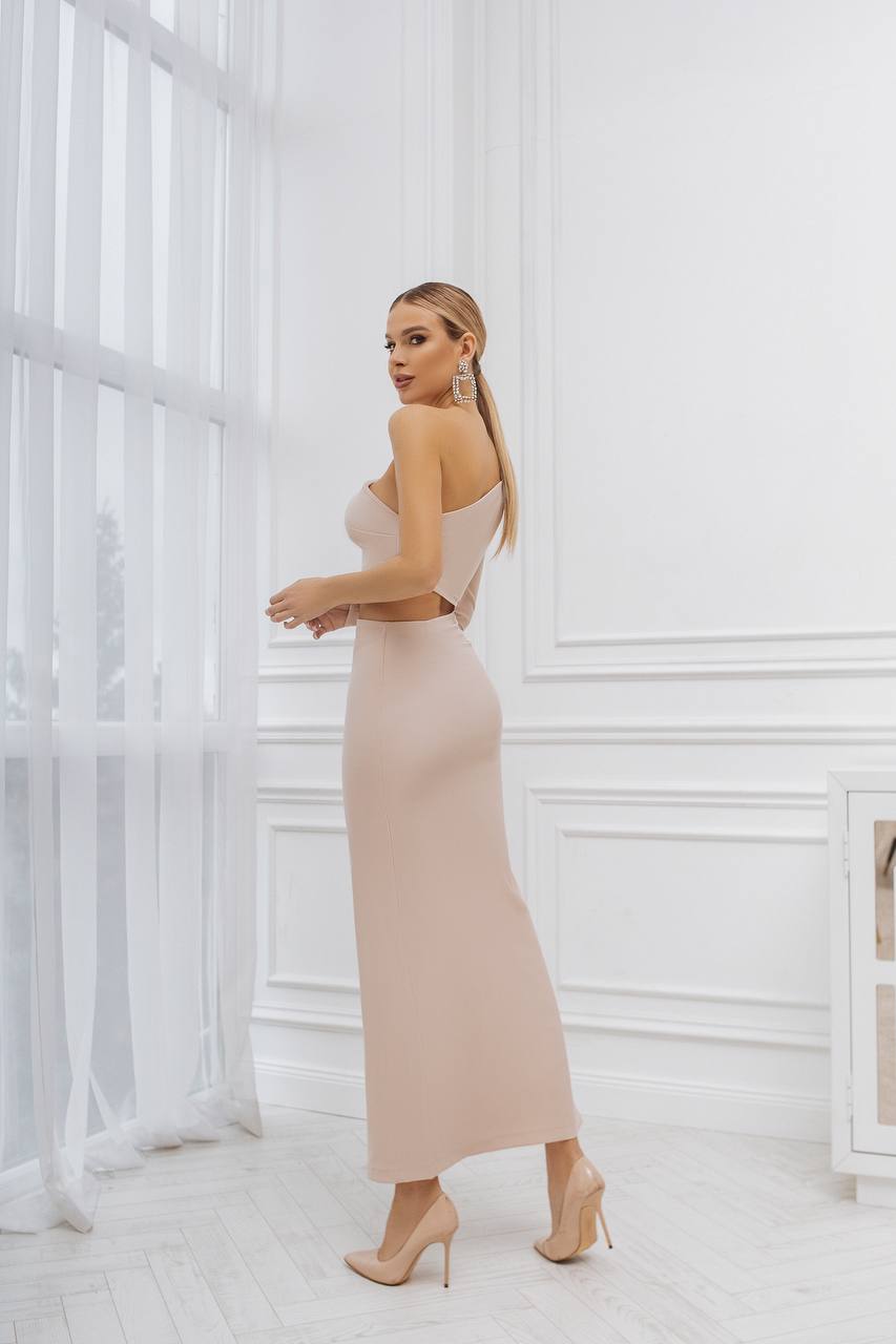 Woman in a beige dress standing in a room with white walls and floor.