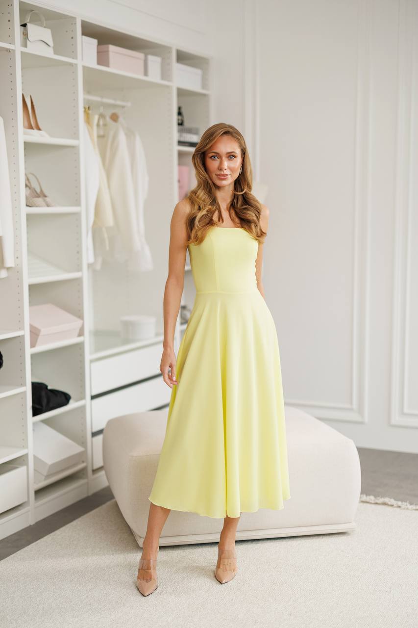 Woman in a light yellow dress standing in a room with white shelves.