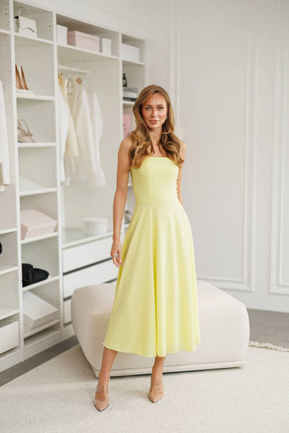 Woman in a light yellow dress standing in a room with white shelves.