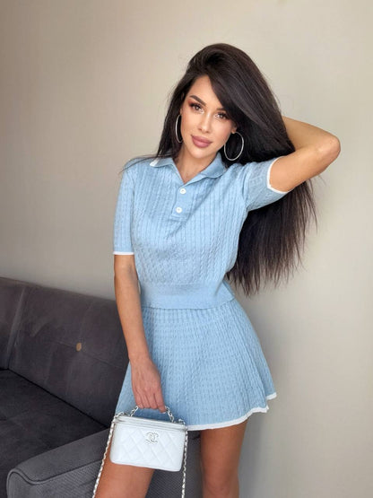 Woman in a light blue dress holding a white handbag against a neutral background