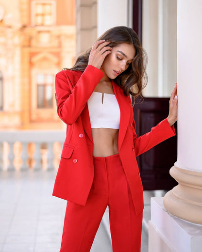 Woman in a red suit standing outdoors with classical architecture in the background