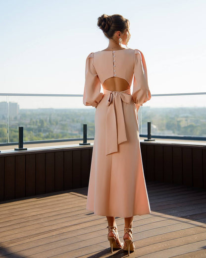 Woman in a long, light pink dress standing on a rooftop with a cityscape view.