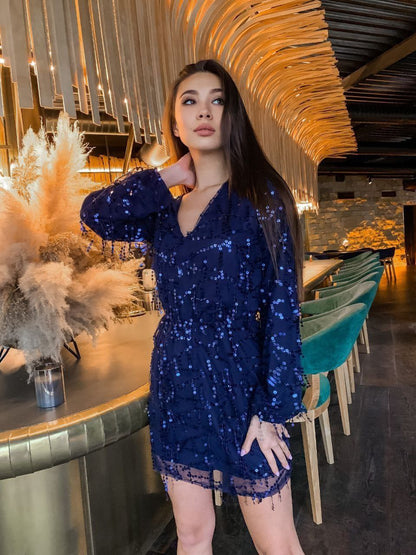 Woman in a blue sequin dress standing in an elegant indoor setting with decorative elements.