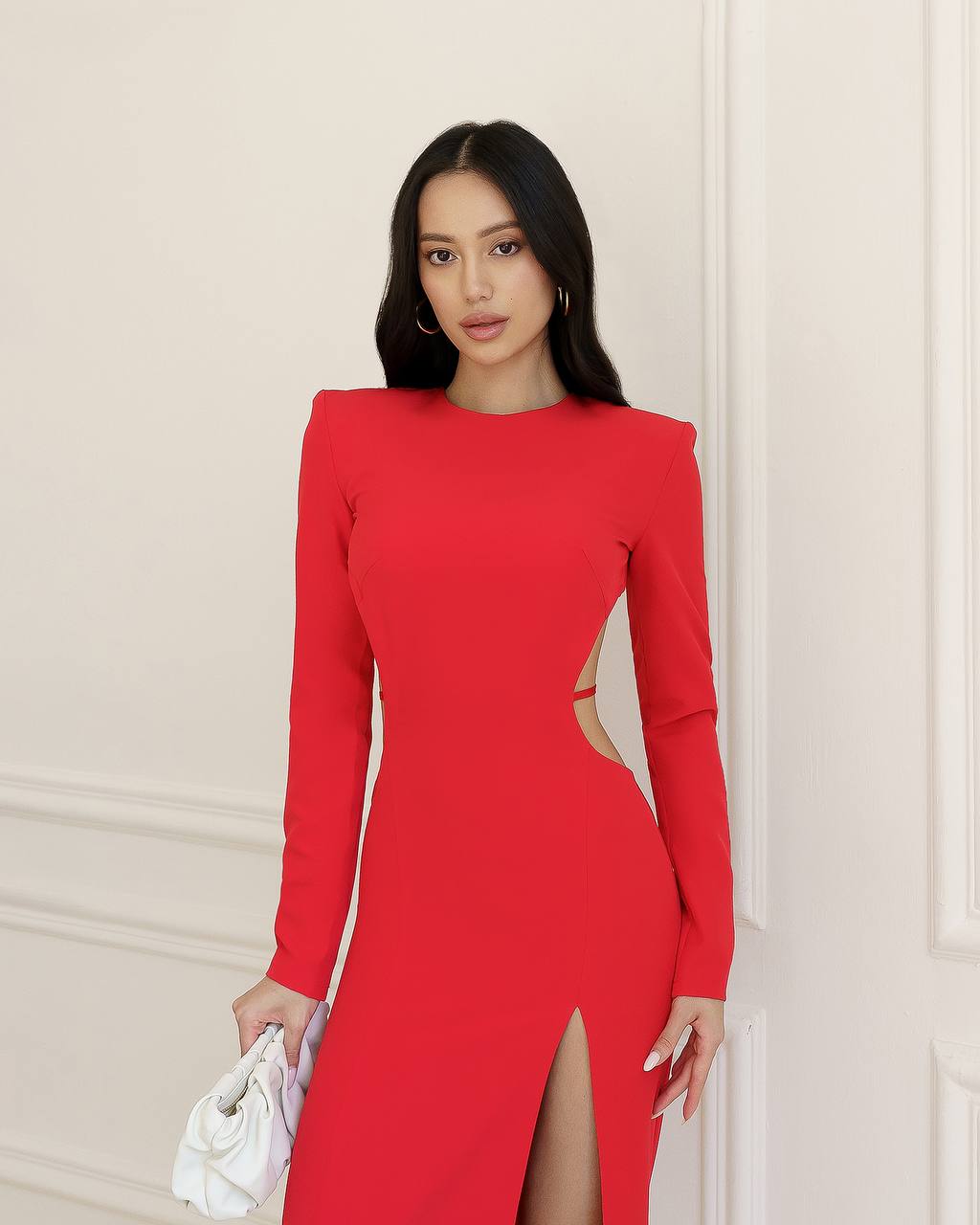 Woman wearing a red dress with cut-out design against a beige wall.