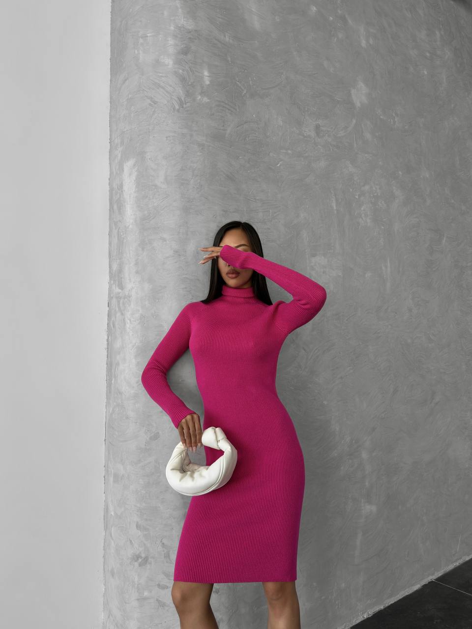 Woman in a bright pink dress standing against a gray wall.