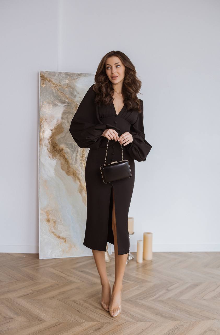 Woman in a black outfit holding a handbag in a minimalistic room with a large abstract painting.