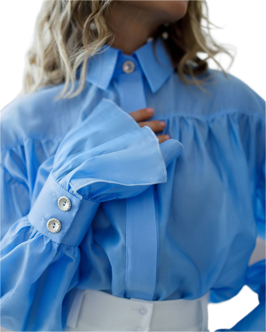 Close-up of a person wearing a blue blouse with ruffled sleeves and buttons.