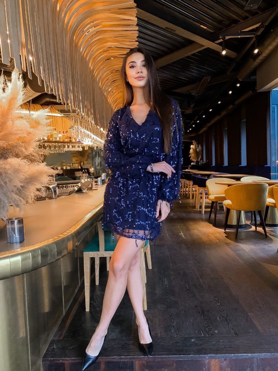 Woman in a blue sequin dress standing in a modern restaurant.