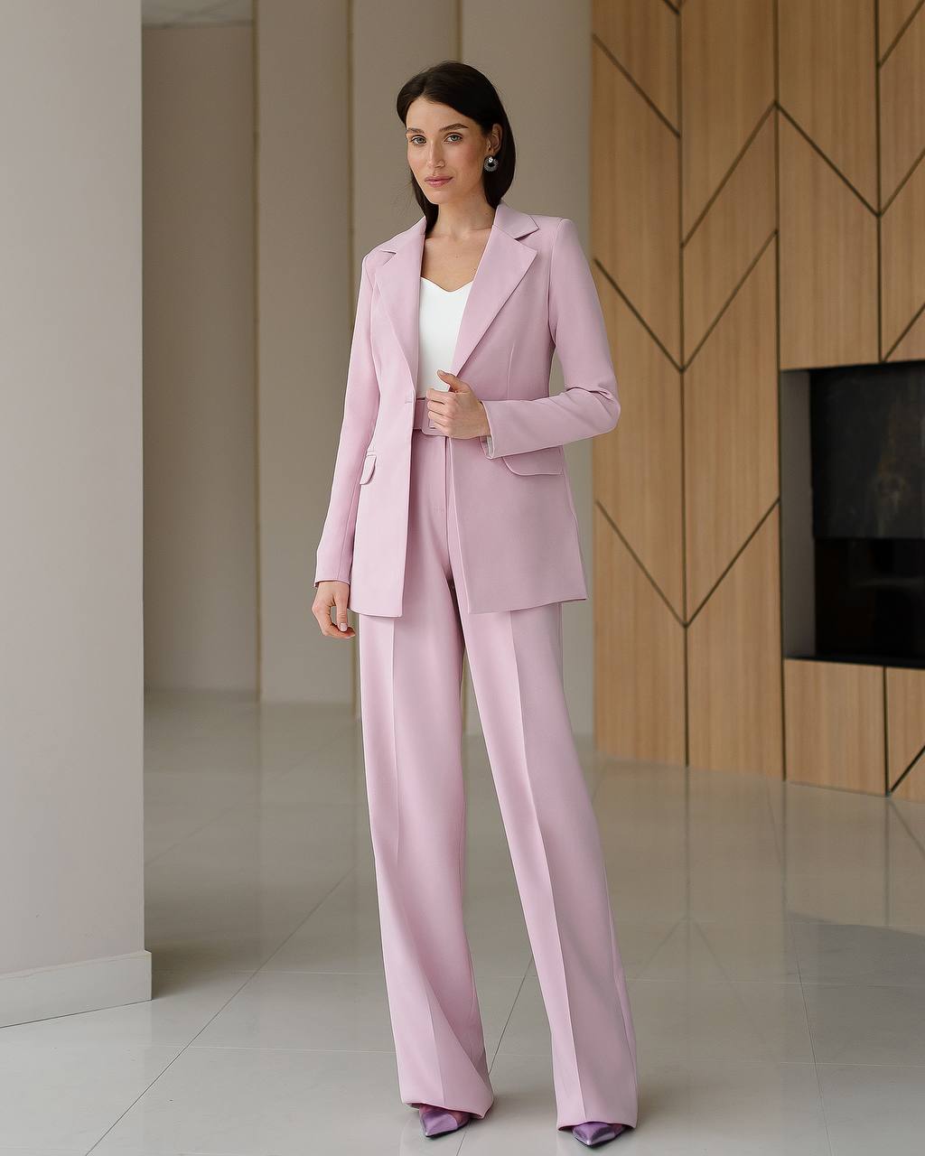 Woman wearing a pink suit standing in a modern interior setting.