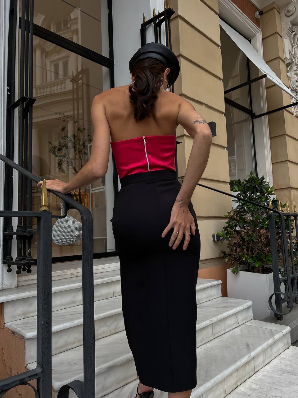 Person wearing a red top and black skirt standing on steps outside a building.