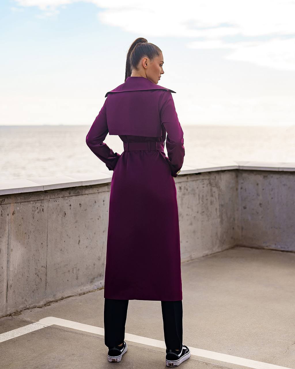 Person wearing a long purple coat standing on a rooftop with a clear sky.