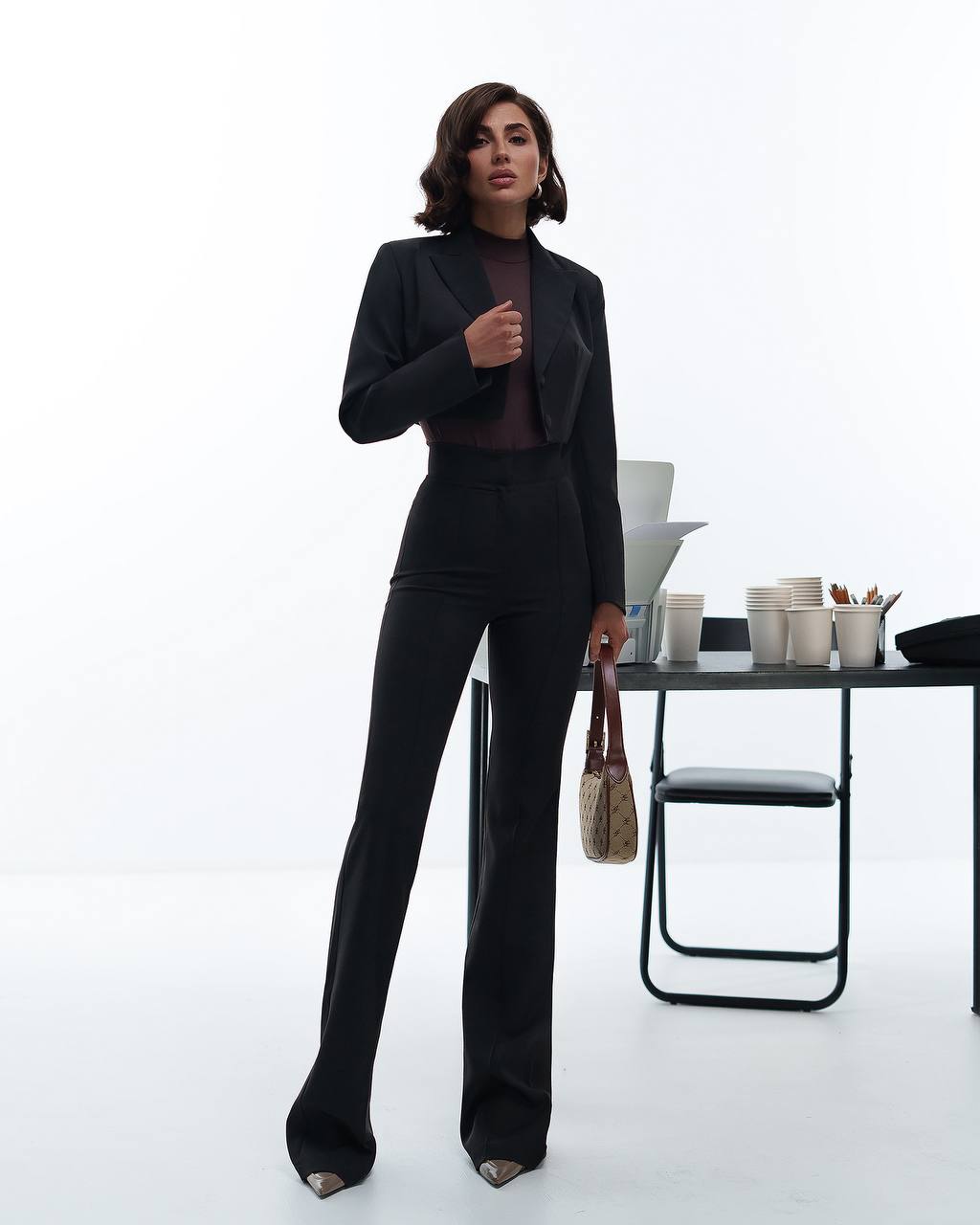 Woman in a black suit standing in an office setting with a white background