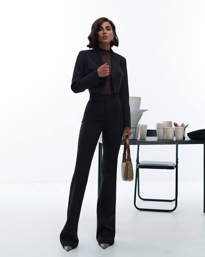 Woman in a black suit standing in an office setting with a white background