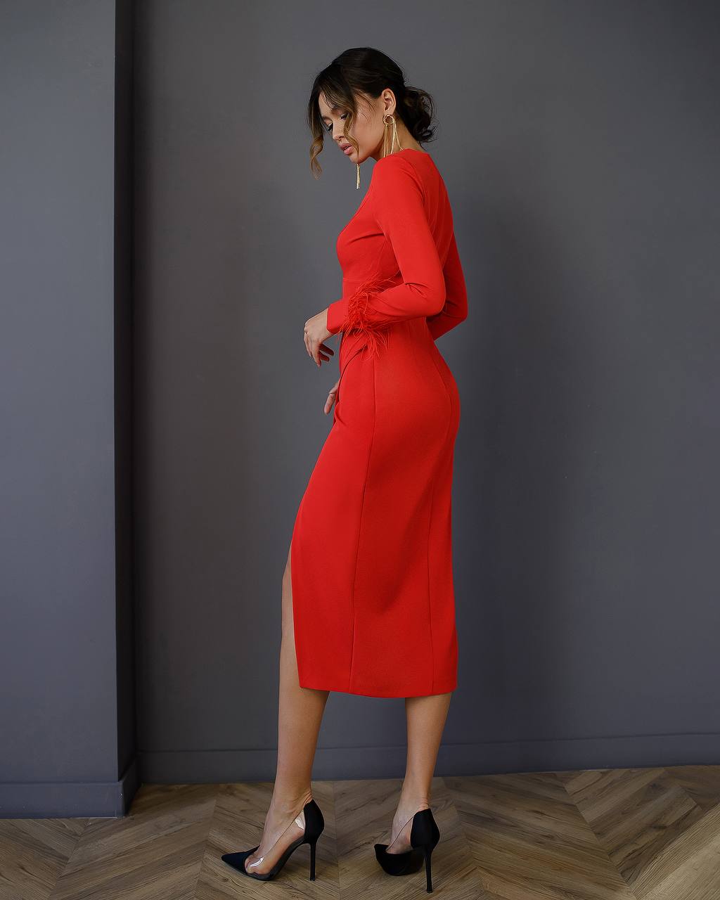 Woman in a red dress standing against a gray wall.
