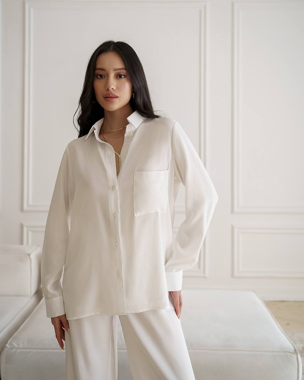 Woman wearing a white shirt and pants in a minimalistic room.