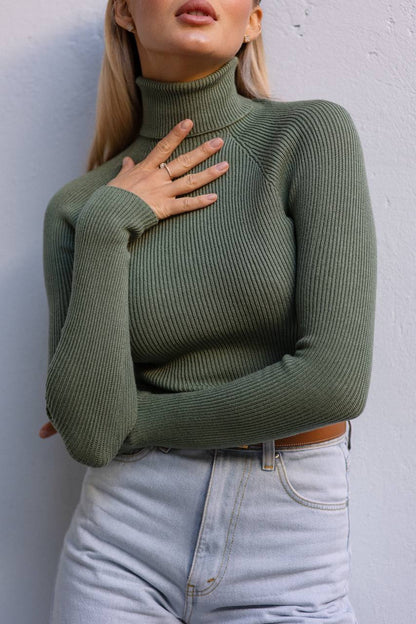 Person wearing a green ribbed sweater against a white wall