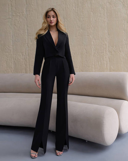 Woman in a black suit standing in a modern interior setting with a beige sofa.