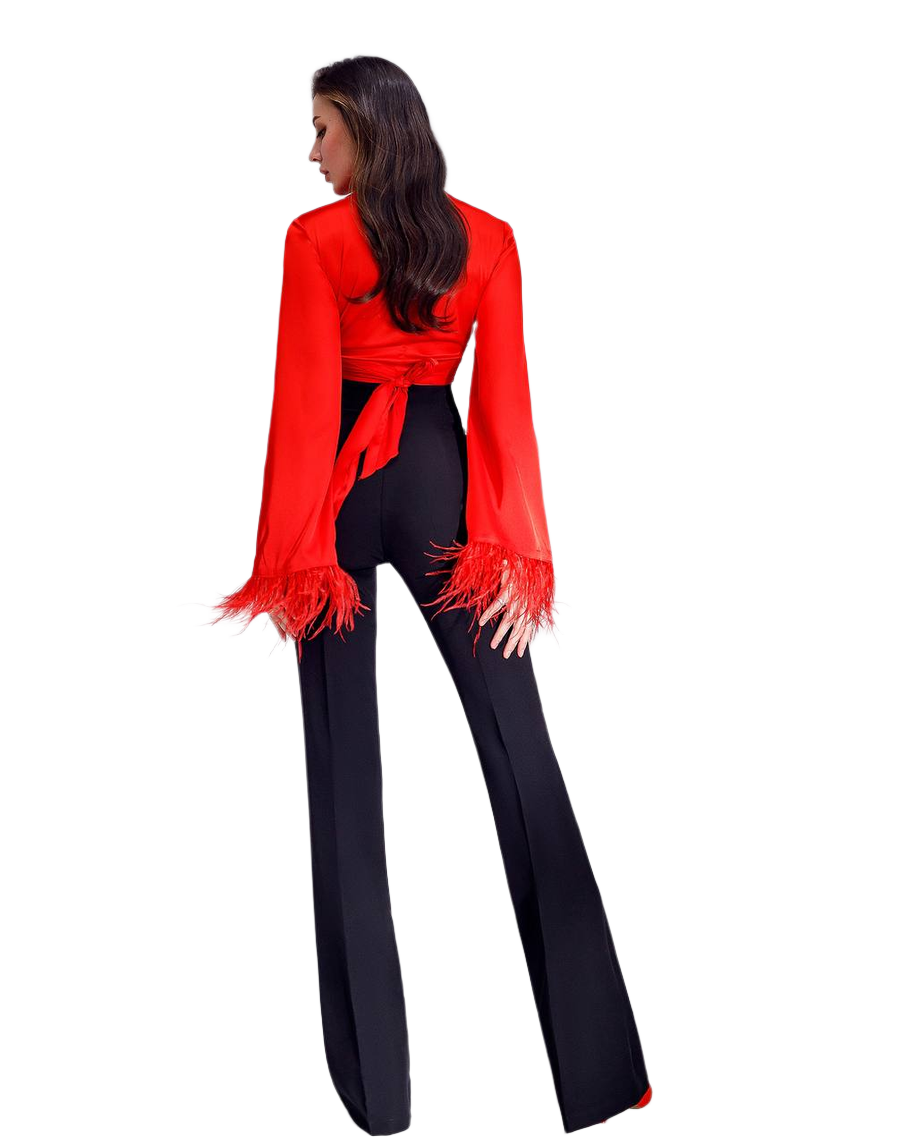 Woman wearing a red blouse with fringe details and black pants on a white background