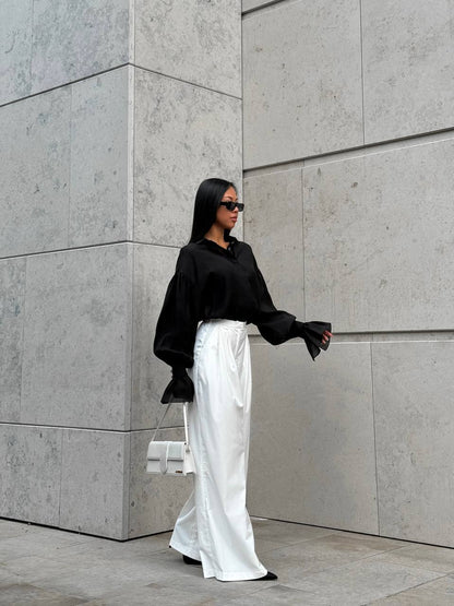 Person wearing a black shirt and white pants standing against a gray concrete wall.