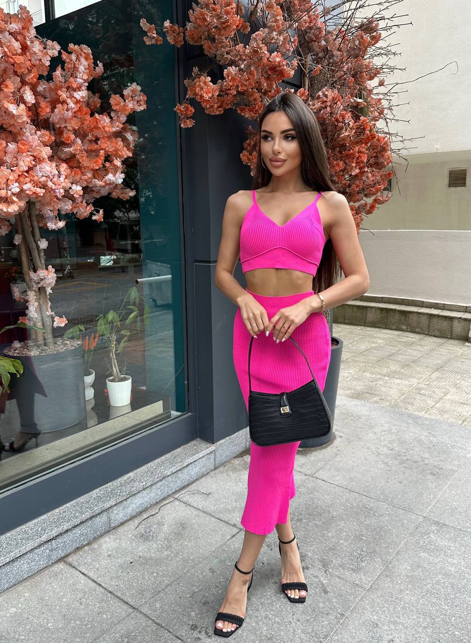 Woman in a bright pink outfit standing outside a building with decorative plants.
