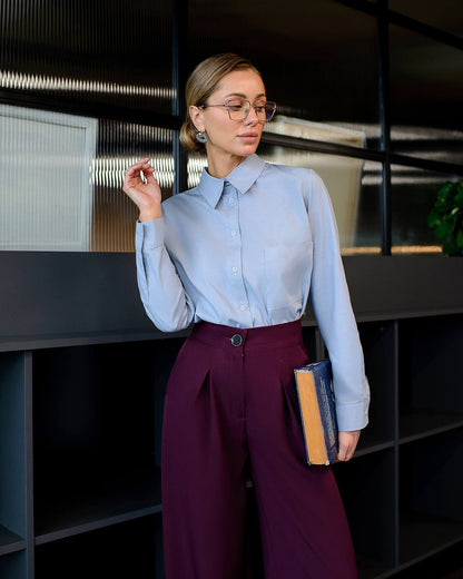 Woman in light blue shirt and dark purple pants holding a book in an indoor setting