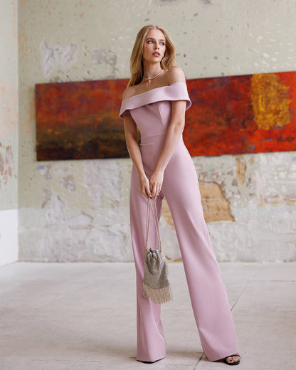 Woman in a pink off-shoulder jumpsuit standing in a room with a colorful abstract painting on the wall.