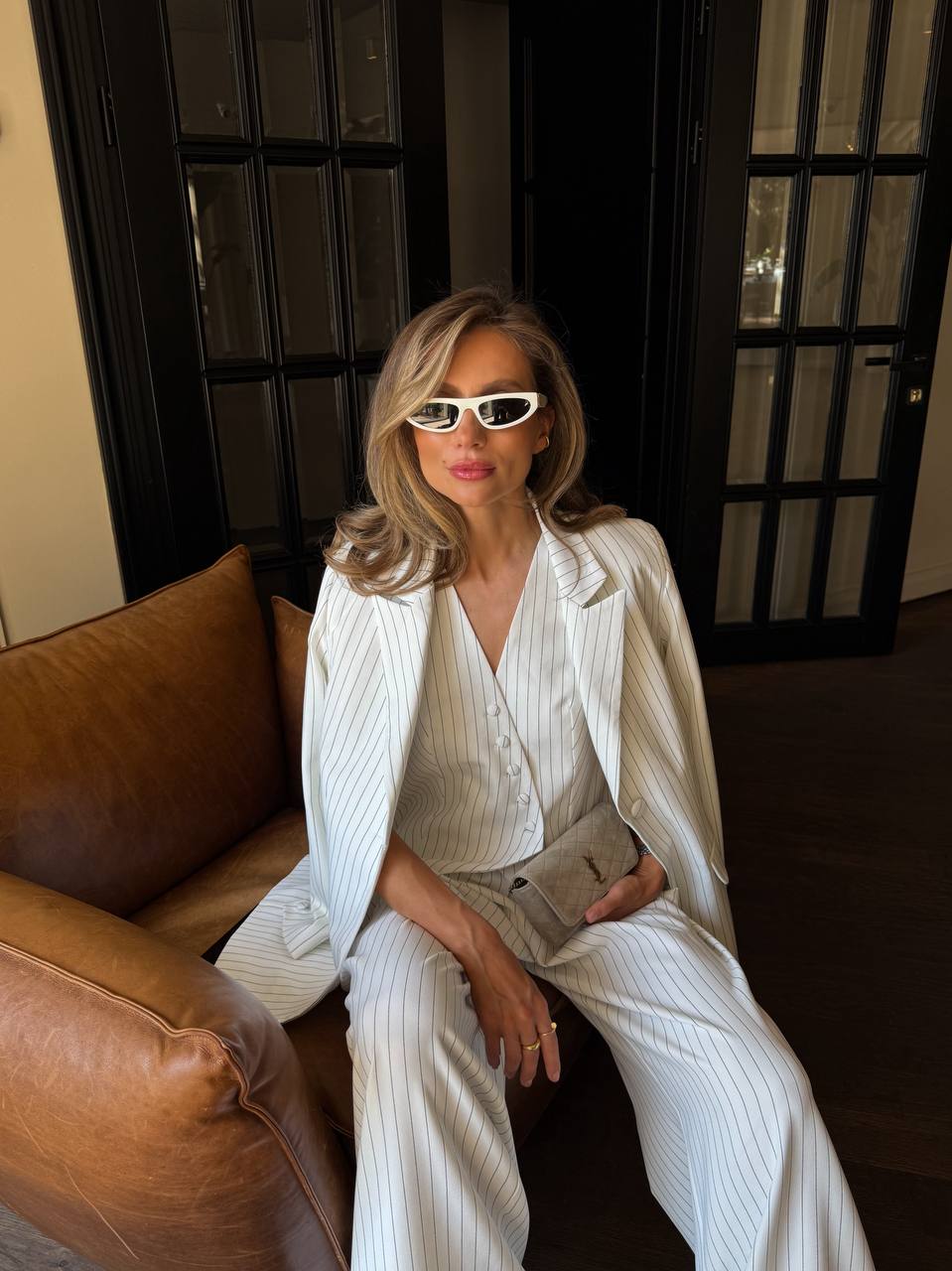 Woman in a white outfit sitting on a brown couch with a dark background