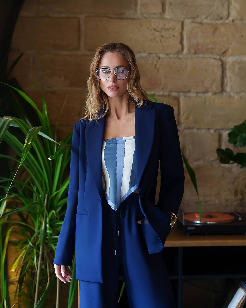 Woman in a blue suit standing in front of a brick wall with plants.