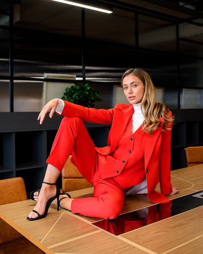 Woman in a red suit sitting on a desk in an office setting