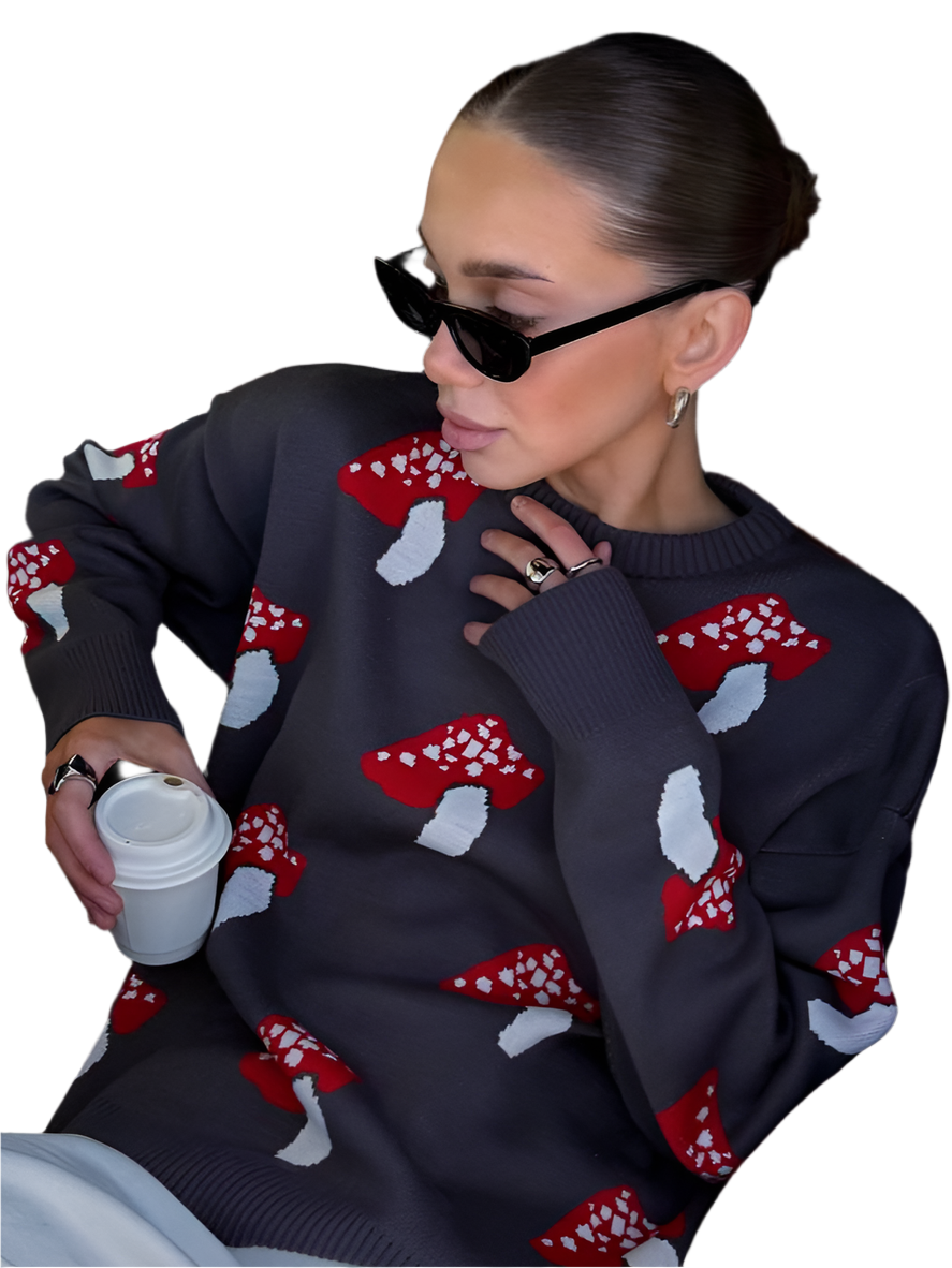 Person wearing a dark sweater with red and white mushroom patterns, holding a white cup.