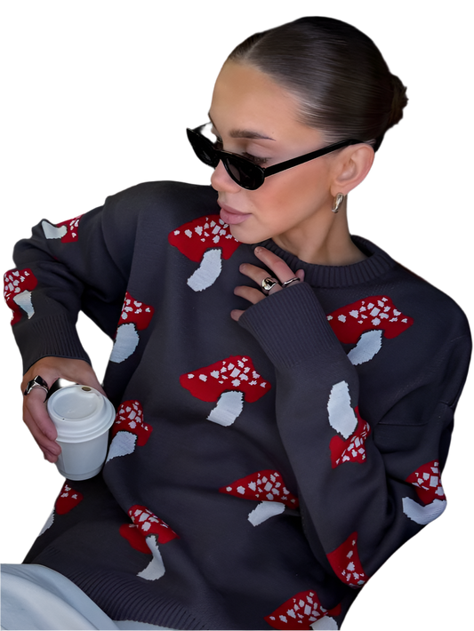 Person wearing a dark sweater with red and white mushroom patterns, holding a white cup.