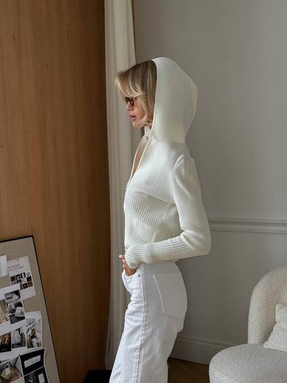 Person wearing a white hoodie and pants in a room with a wooden wall and a chair.