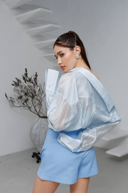 Woman wearing a light blue outfit with a sheer overlay in a minimalistic setting.