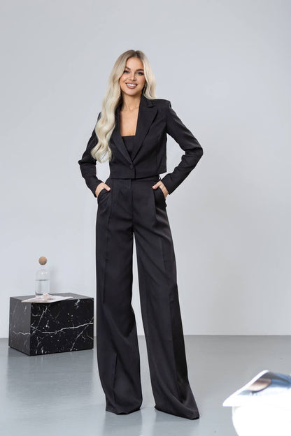 Woman wearing a black suit standing against a plain background