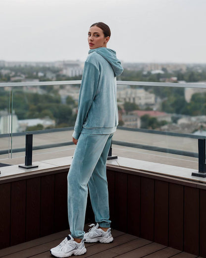 Person wearing a light blue tracksuit standing on a rooftop with a cityscape in the background