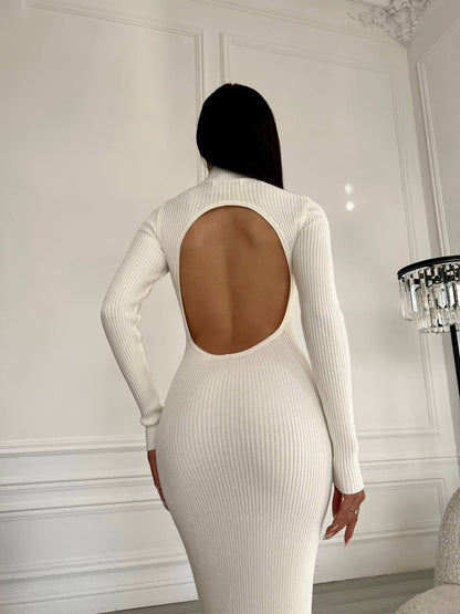 Person wearing a white ribbed dress with an open back in a room with white walls and a chandelier.