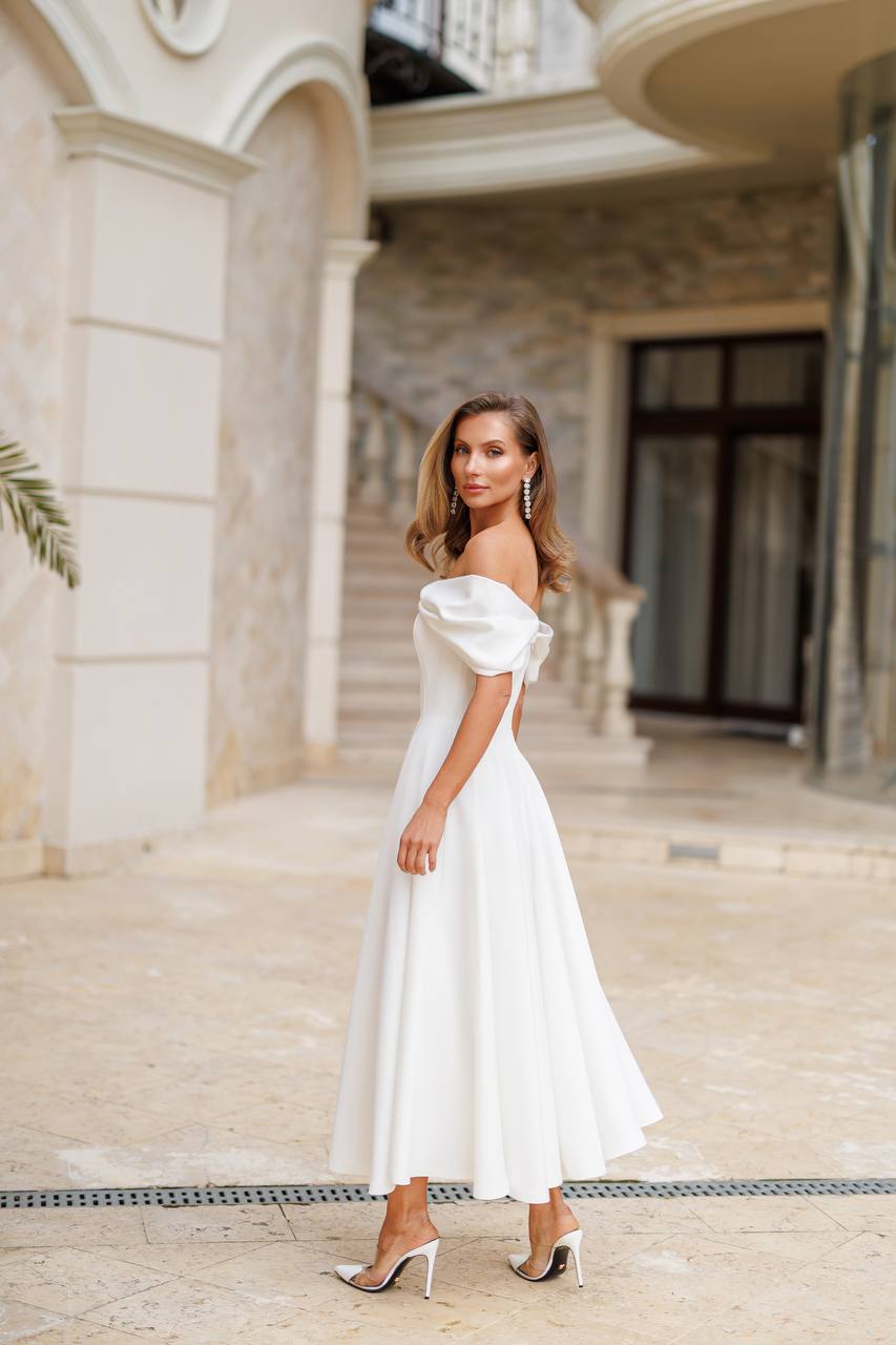 Woman in a white off-shoulder dress standing in front of an elegant building.