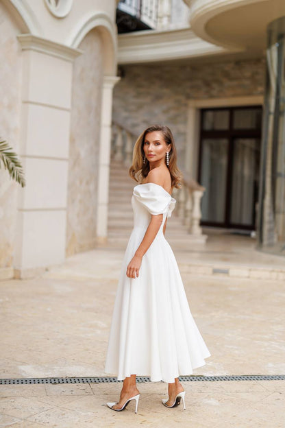 Woman in a white off-shoulder dress standing in front of an elegant building.